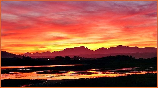 Winter sunset reflecting in the Swartvlei Lagoon and silhouetting the Outeniqua Mountains.